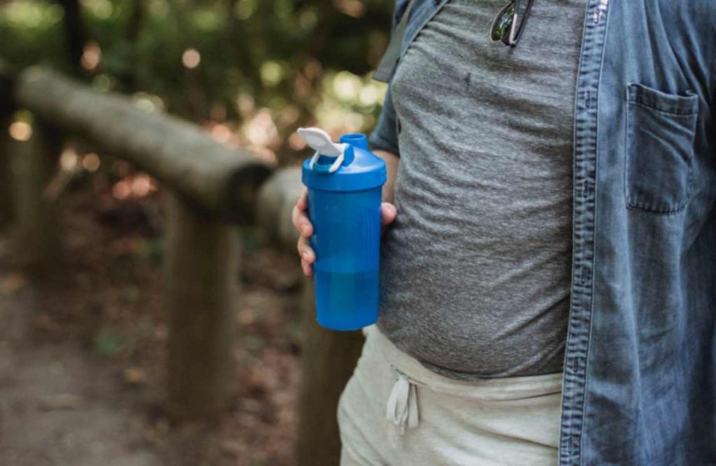Bring sufficient water when hiking. The picture shows someone holding a water bottle with liquid in it.