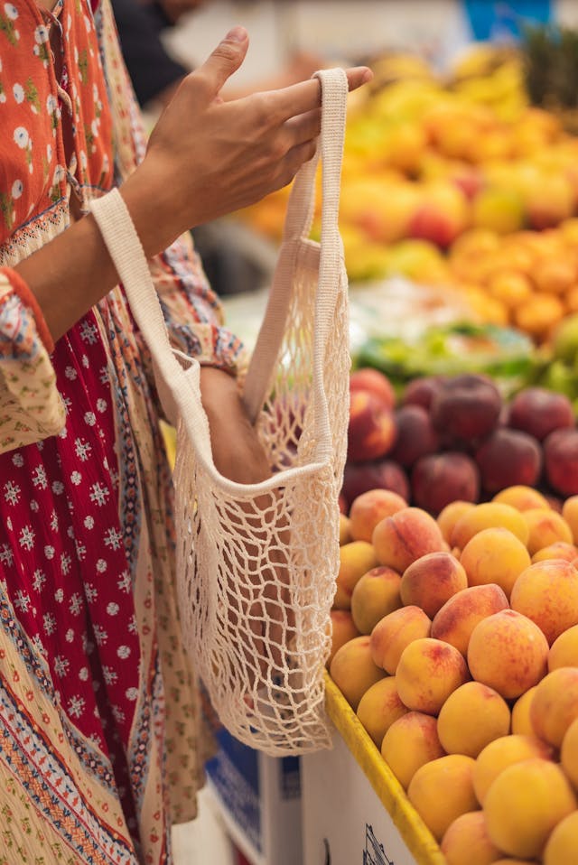 A lady holding a reusable mesh shopping bag for loose vegetables.