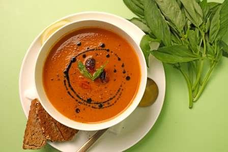 A bowl of soup on a green surface with leaves next to it.
